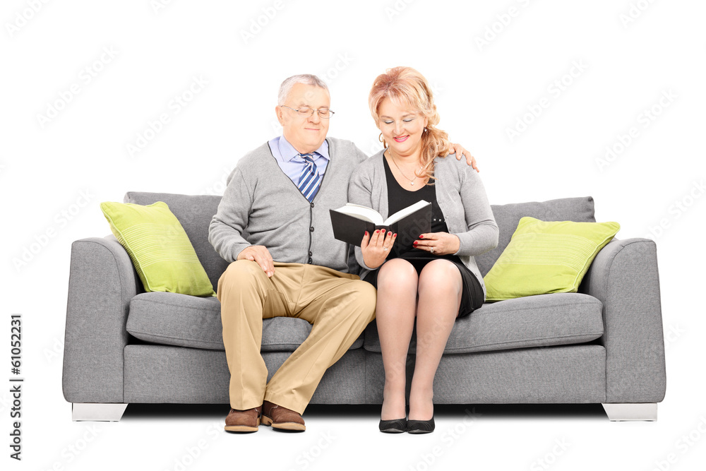 Middle aged couple seated on sofa reading a book