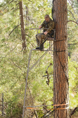 Bow hunter demonstrating good safety technique using a haul line to bring up his bow into a ladder style tree stand