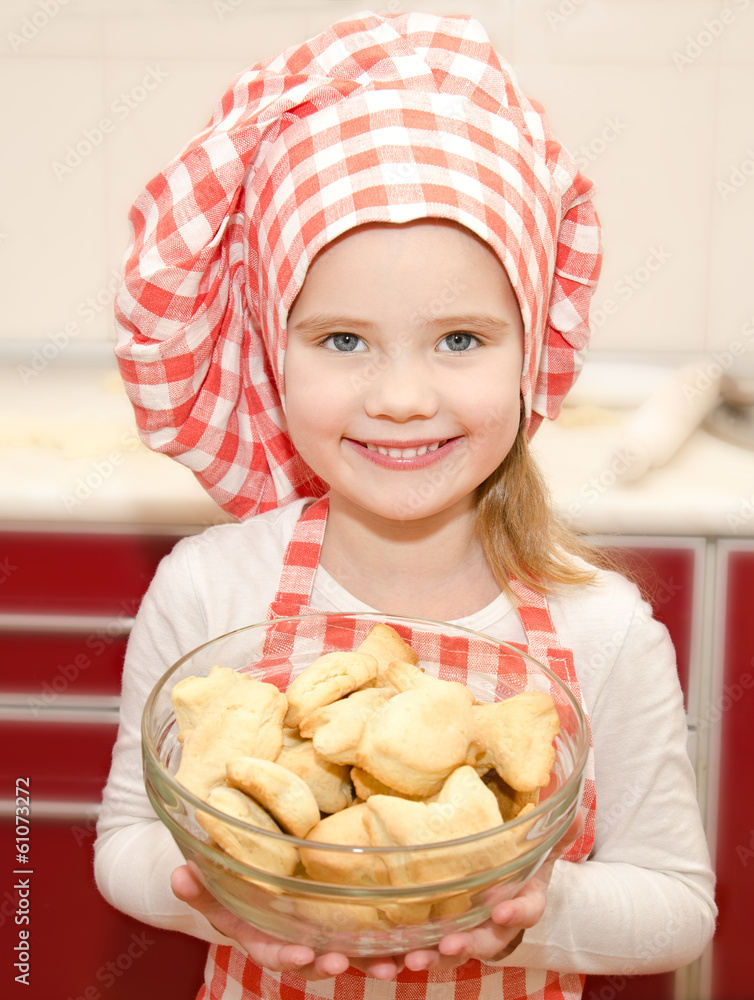 Smiling little girl in chef hat holding bowl with cookies Smiling little girl in chef hat holding bowl with cookies