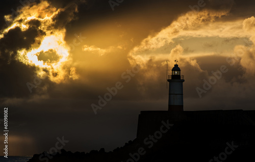 Beautiful vibrant sunrise sky over calm water ocean with lightho