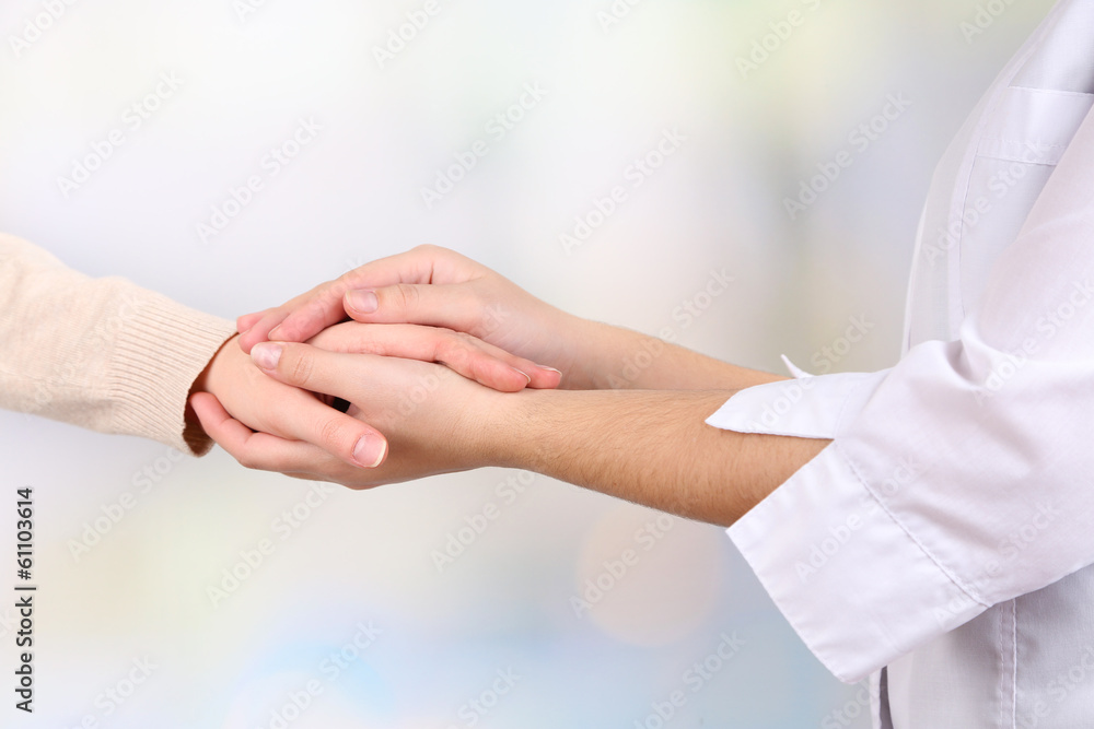 Medical doctor holding hand of patient, on light background Medical doctor holding hand of patient, on light background