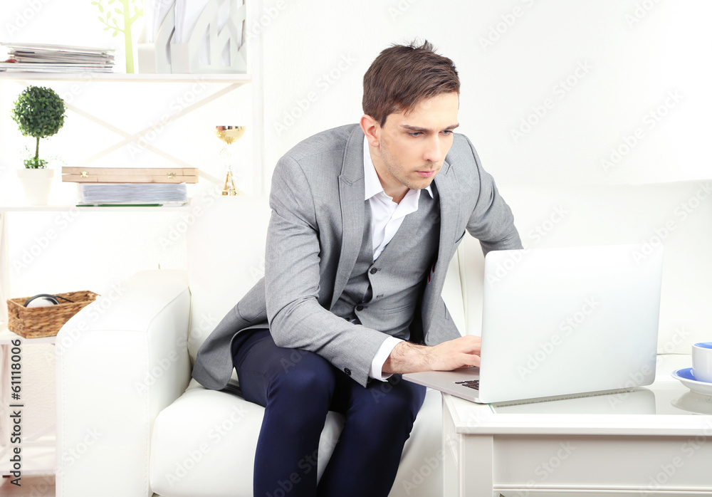 Young businessman sitting on sofa and using laptop at home Young businessman sitting on sofa and using laptop at home