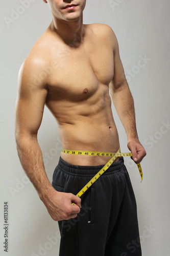 Shirtless fit young man measuring his waist