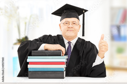College professor seated on table with books gesturing happiness