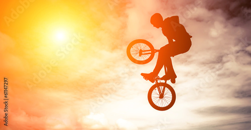 Fotografiet Man doing an jump with a bmx bike against sunshine sky.