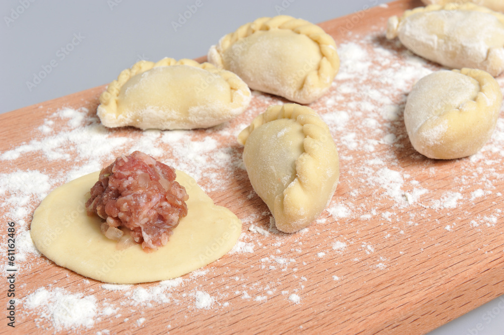 Uncooked floured pelmeni with a pattern on the cutting board on Uncooked floured pelmeni with a pattern on the cutting board on