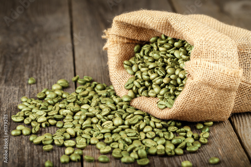 Green coffee beans in bag made from burlap on wooden surface