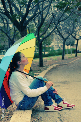 Young woman looks at the sun under a big rainbow umbrella