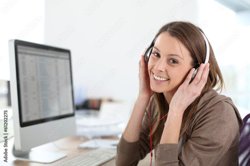 Woman in front of desktop computer with headphones Woman in front of desktop computer with headphones