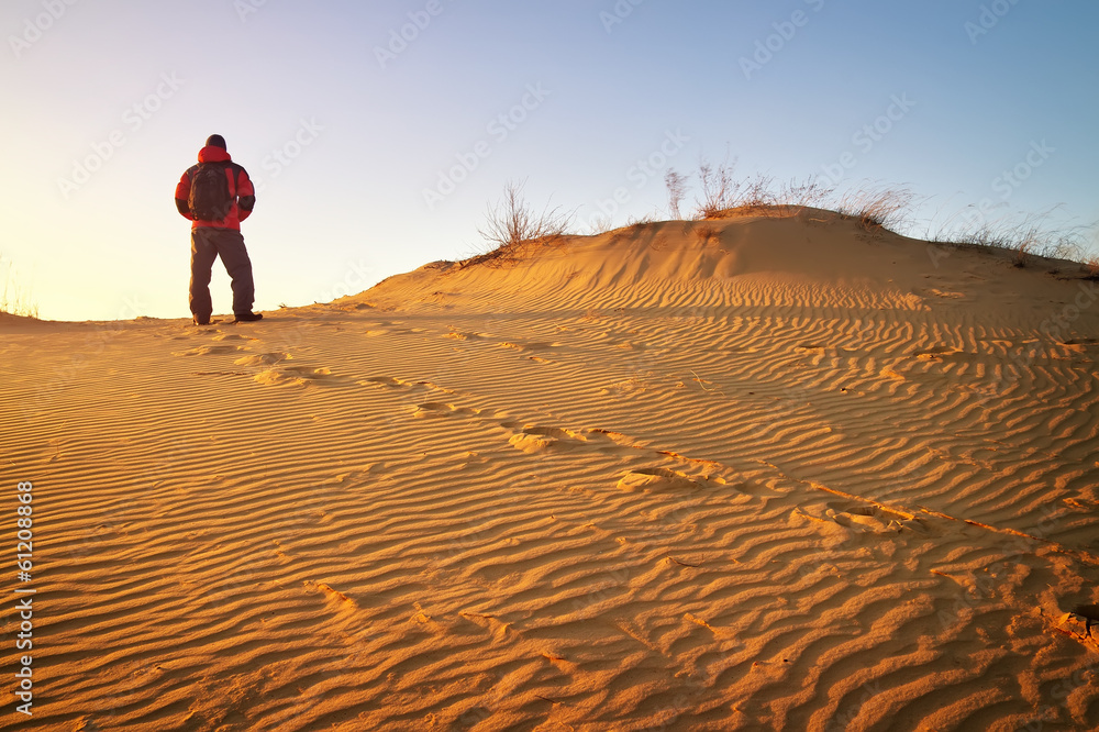 Sandy desert and man in winter clothes standing at a dune top