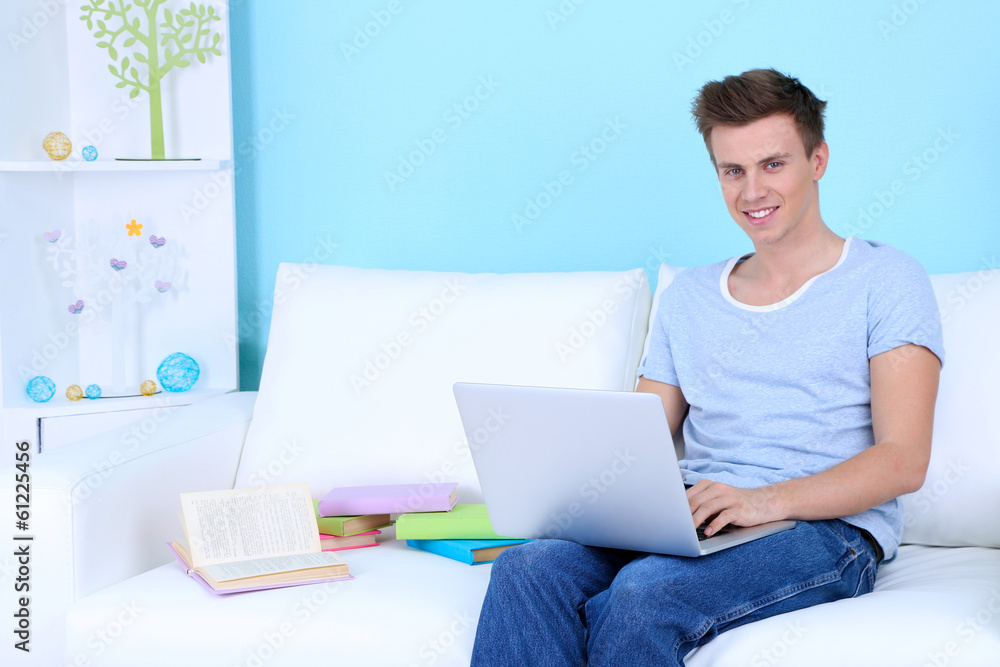 Guy sitting on sofa with laptop on blue background Guy sitting on sofa with laptop on blue background