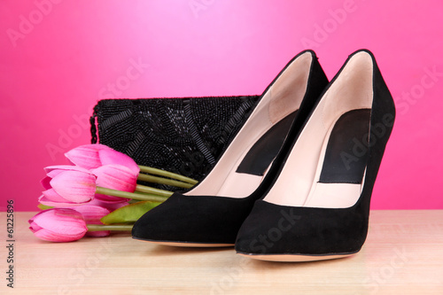 Beautiful black female shoes, bag and flowers on pink
