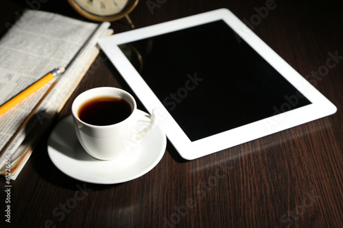 Tablet, newspaper, cup of coffee and alarm clock on wooden