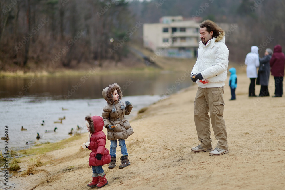 Obraz premium Father and daughters feeding ducks at autumn