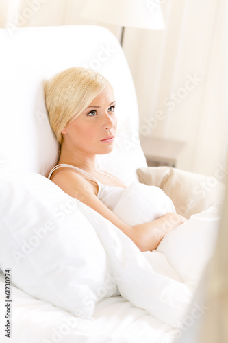 Pensive woman lying in bed under the warm blanket