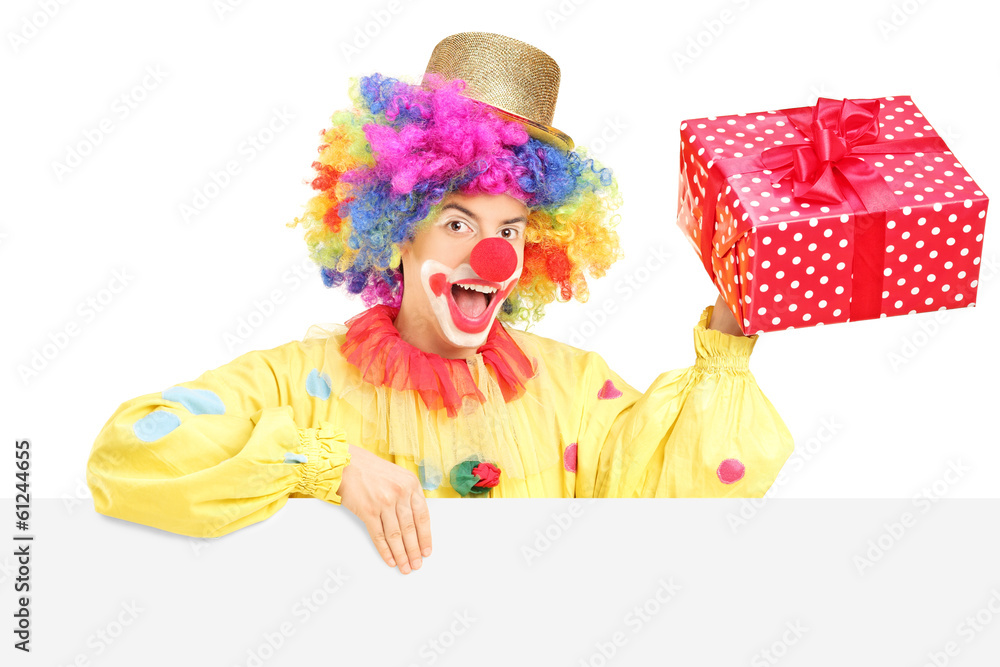 Male clown with cheerful expression holding present behind blank Male clown with cheerful expression holding present behind blank