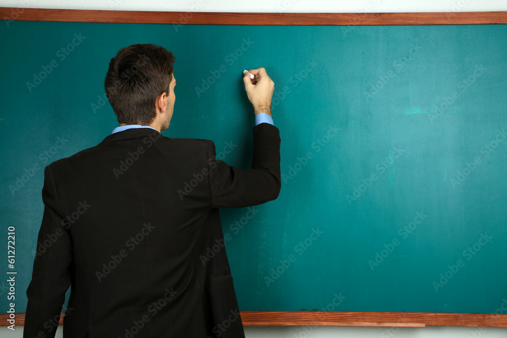 Young teacher near chalkboard in school classroom