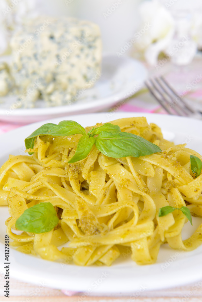 Delicious pasta with pesto on plate on table on light Delicious pasta with pesto on plate on table on light