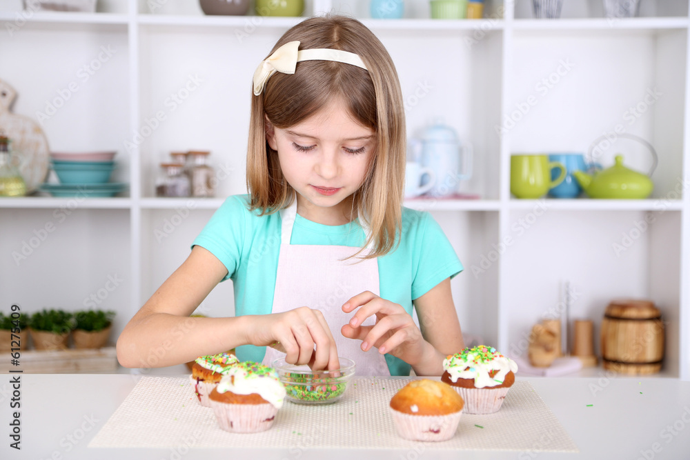 Little girl decorating cupcakes in kitchen at home