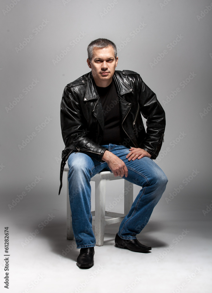 Sexy adult man in leather jacket sitting on white chair Sexy adult man in leather jacket sitting on white chair