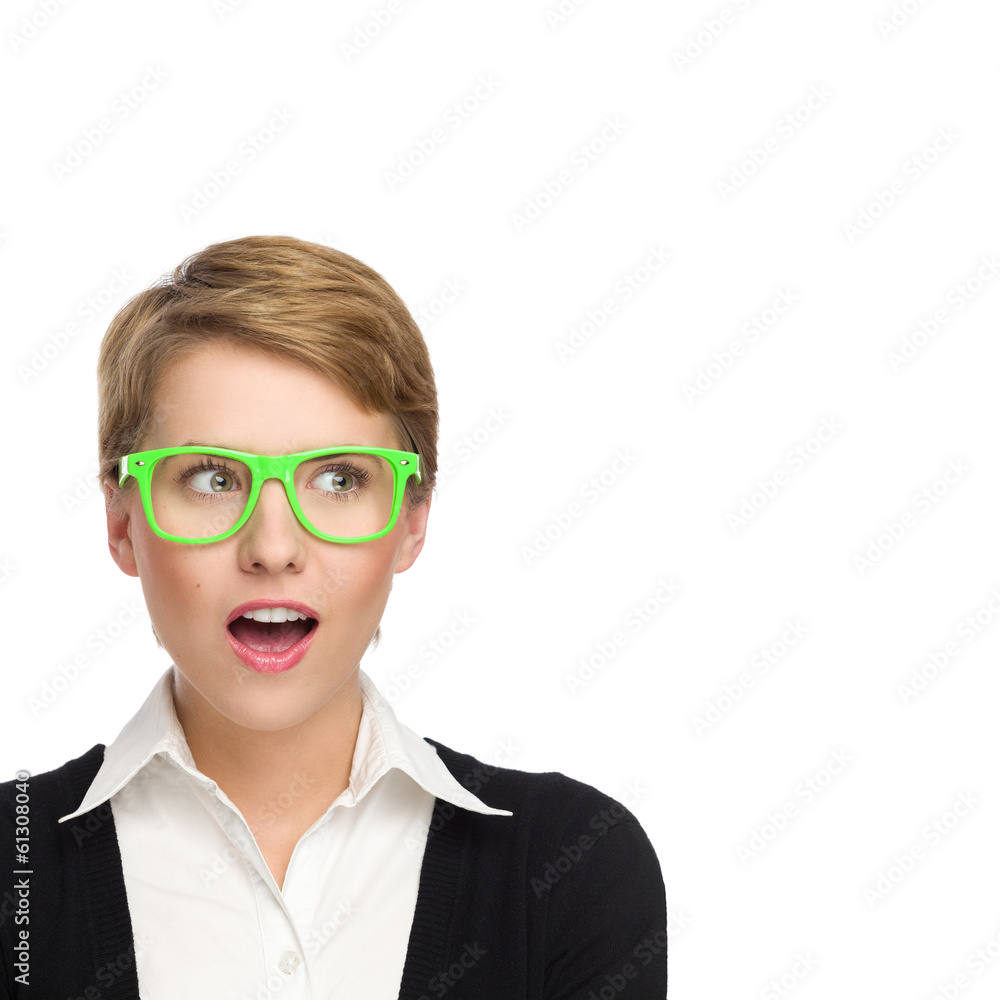 Surprised young woman in green glasses looking at copy space.