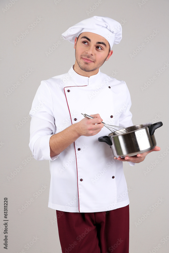 Professional chef in white uniform and hat, holding pan in his Professional chef in white uniform and hat, holding pan in his