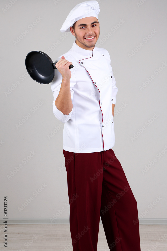 Professional chef in white uniform and hat, holding pan in his Professional chef in white uniform and hat, holding pan in his
