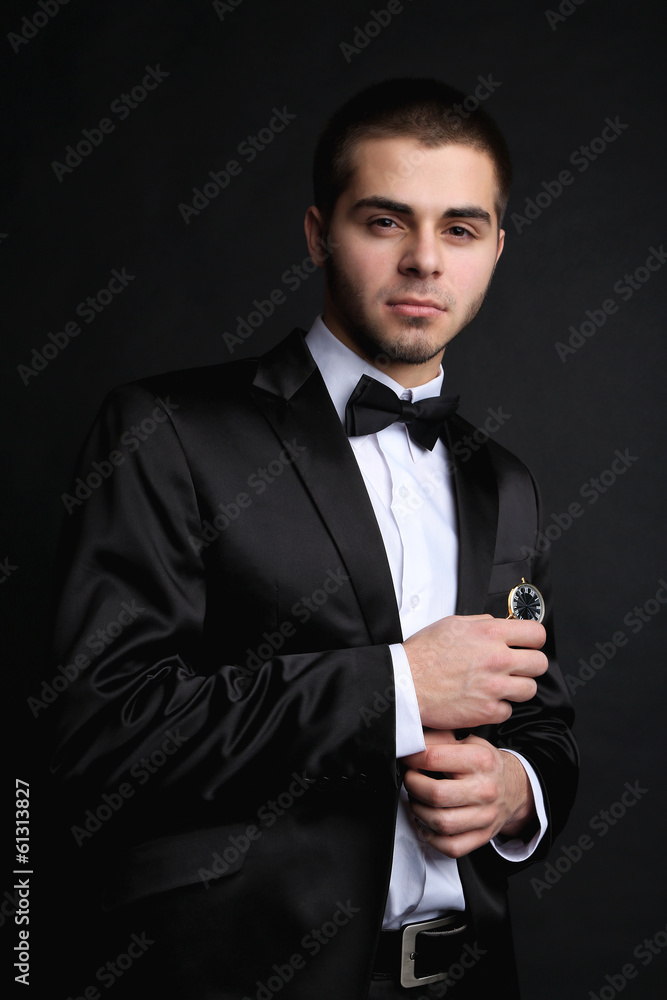 Handsome young man in suit holding watch on dark background Handsome young man in suit holding watch on dark background