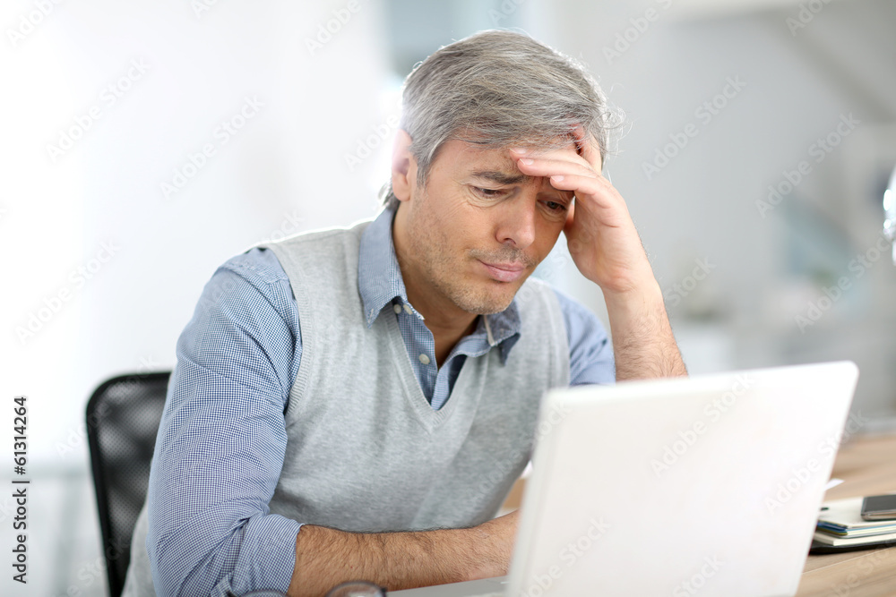 Senior businessman in front of laptop having a headache Senior businessman in front of laptop having a headache
