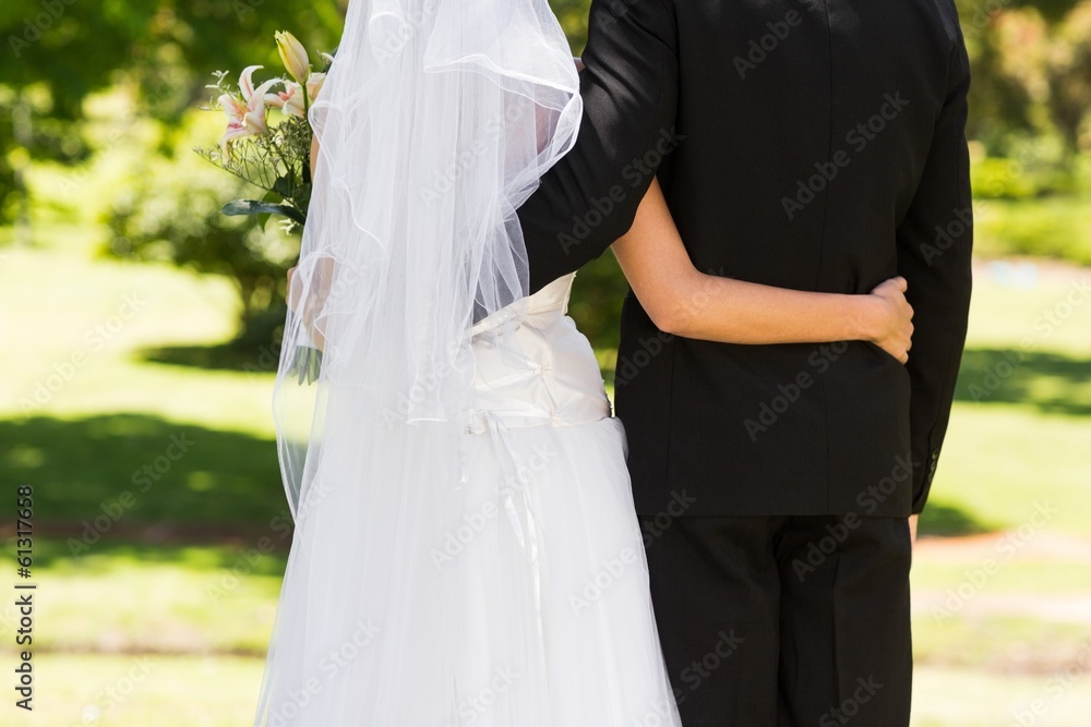 Mid section of a newlywed with arms around in park