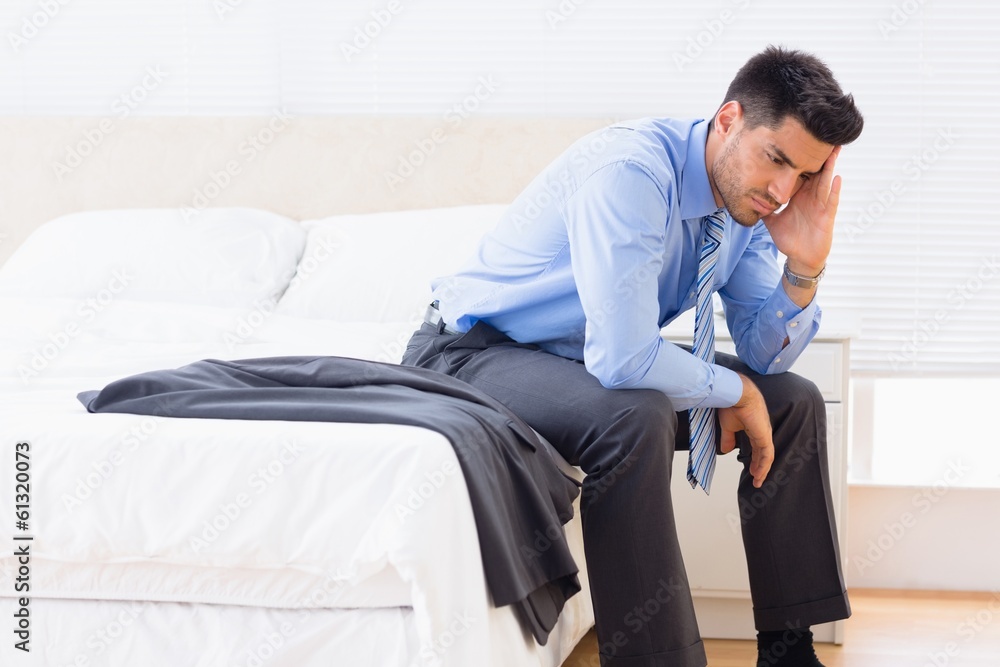 Frowning businessman sitting at edge of bed