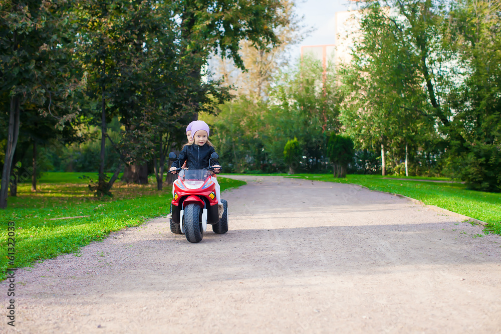Adorable little girls riding on kid's motobike in the green park Adorable little girls riding on kid's motobike in the green park