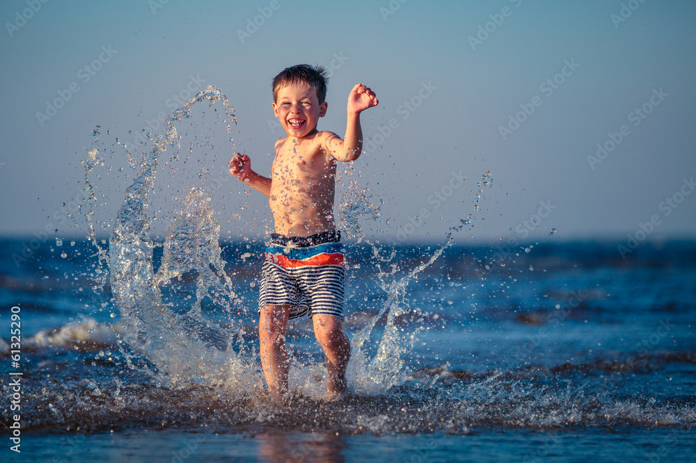 Fototapeta premium Little boy running through the water at beach