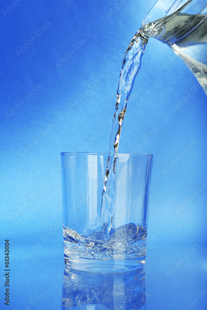 Pour water from pitcher into glass, on dark blue background Pour water from pitcher into glass, on dark blue background