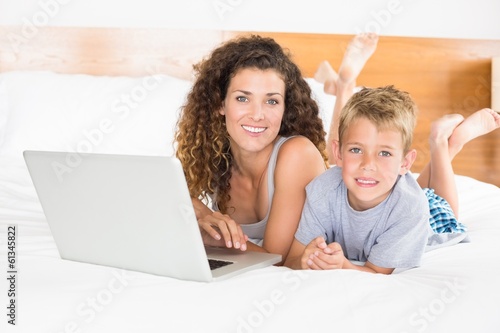 Smiling blonde boy and mother lying on bed using laptop