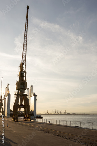 Old crane on the harbor pier during sunset.