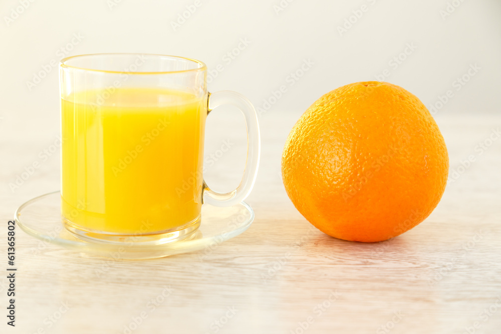 An orange next to a mug with juice An orange next to a mug with juice