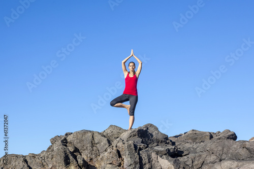 Young woman practicing tree yoga pose outdoor against blue sky