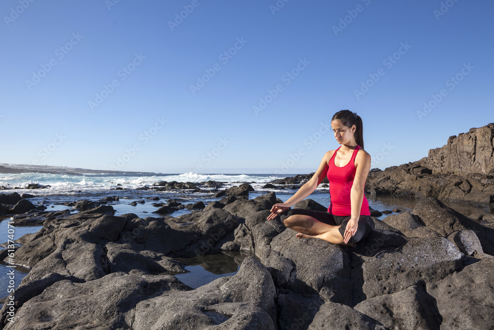 young woman practicing yoga meditation on the beach