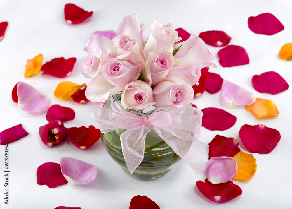 Collection of rose petals with a vase of pink roses in the middl
