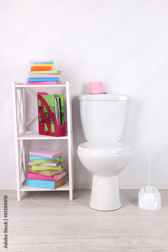 White toilet bowl and stand with books, on color wall White toilet bowl and stand with books, on color wall