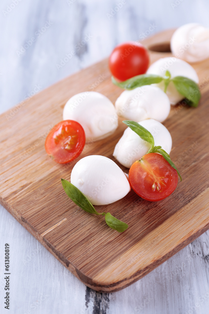 Tasty mozzarella cheese with basil and tomatoes, on wooden Tasty mozzarella cheese with basil and tomatoes, on wooden