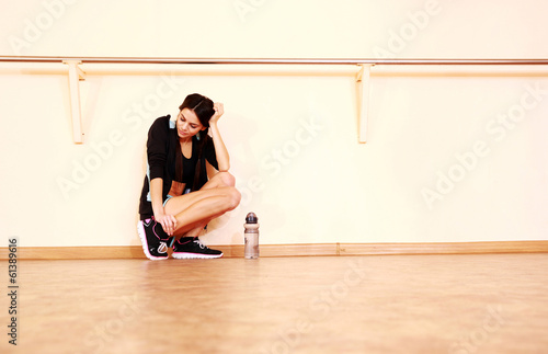 Tired young fit woman leaning on the wall at gym