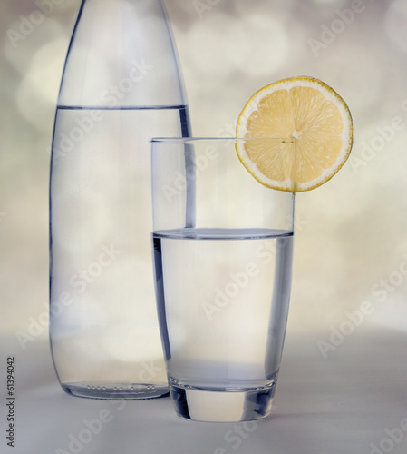 Glass of water with lemon in front of water bottle with bokeh ba photo