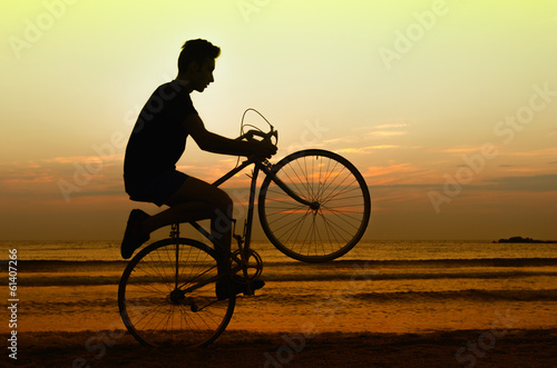Fototapeta Naklejka Na Ścianę i Meble -  Man riding a bicycle at the sunrise on the beach, getting fit