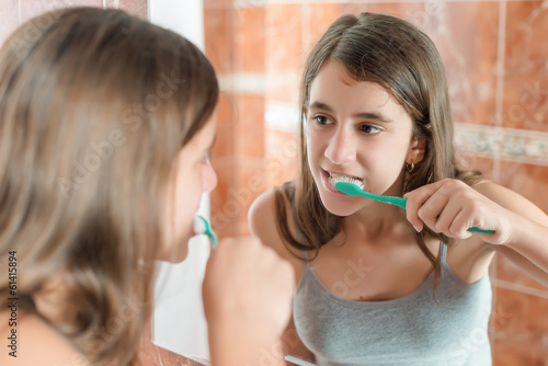 Girl brushing her teeth in front of a mirror photo