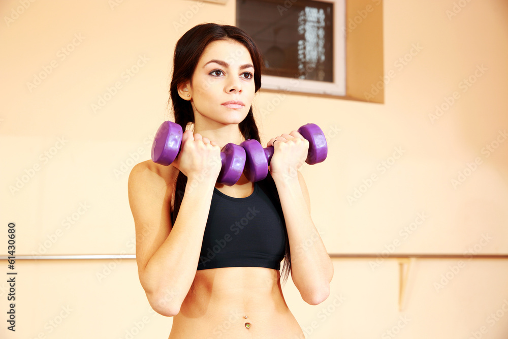 Young thoughtful fit woman doing exercises with dumbells at gym