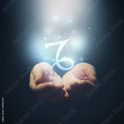 Female hands opening to light and holding zodiac sign for Capric