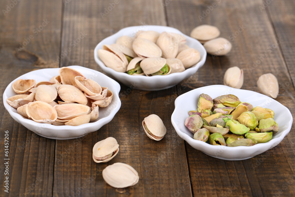 Pistachio nuts in small bowls on wooden background Pistachio nuts in small bowls on wooden background