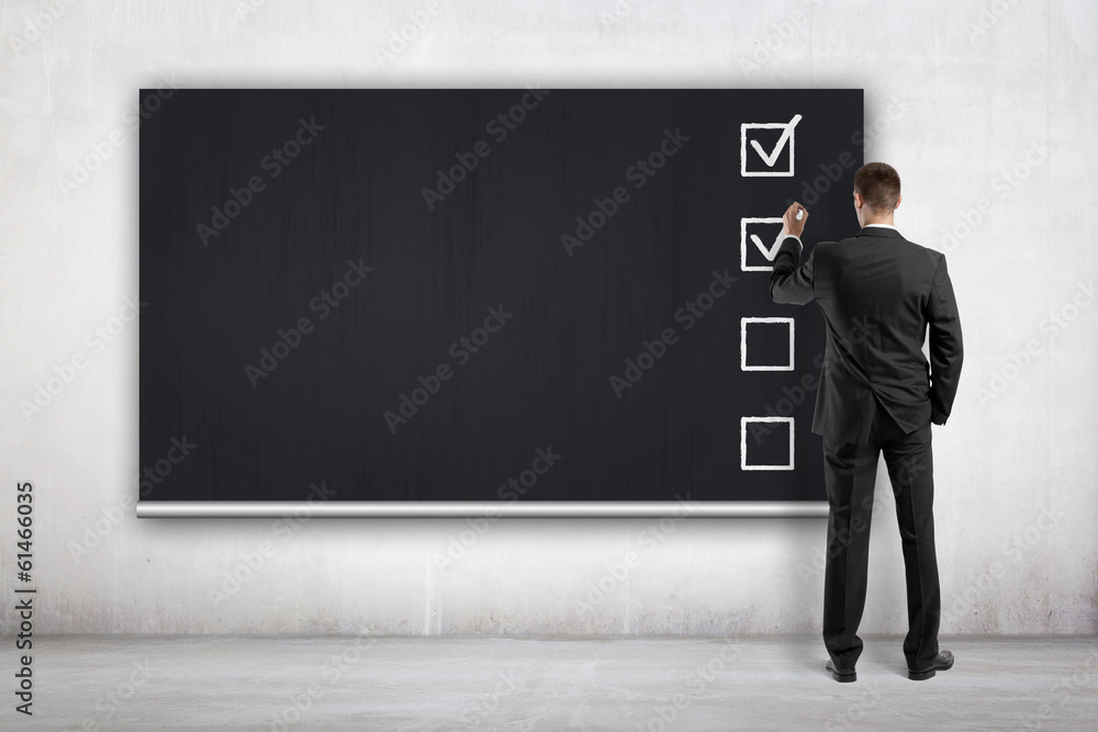 businessman drawing checklist on blackboard businessman drawing checklist on blackboard